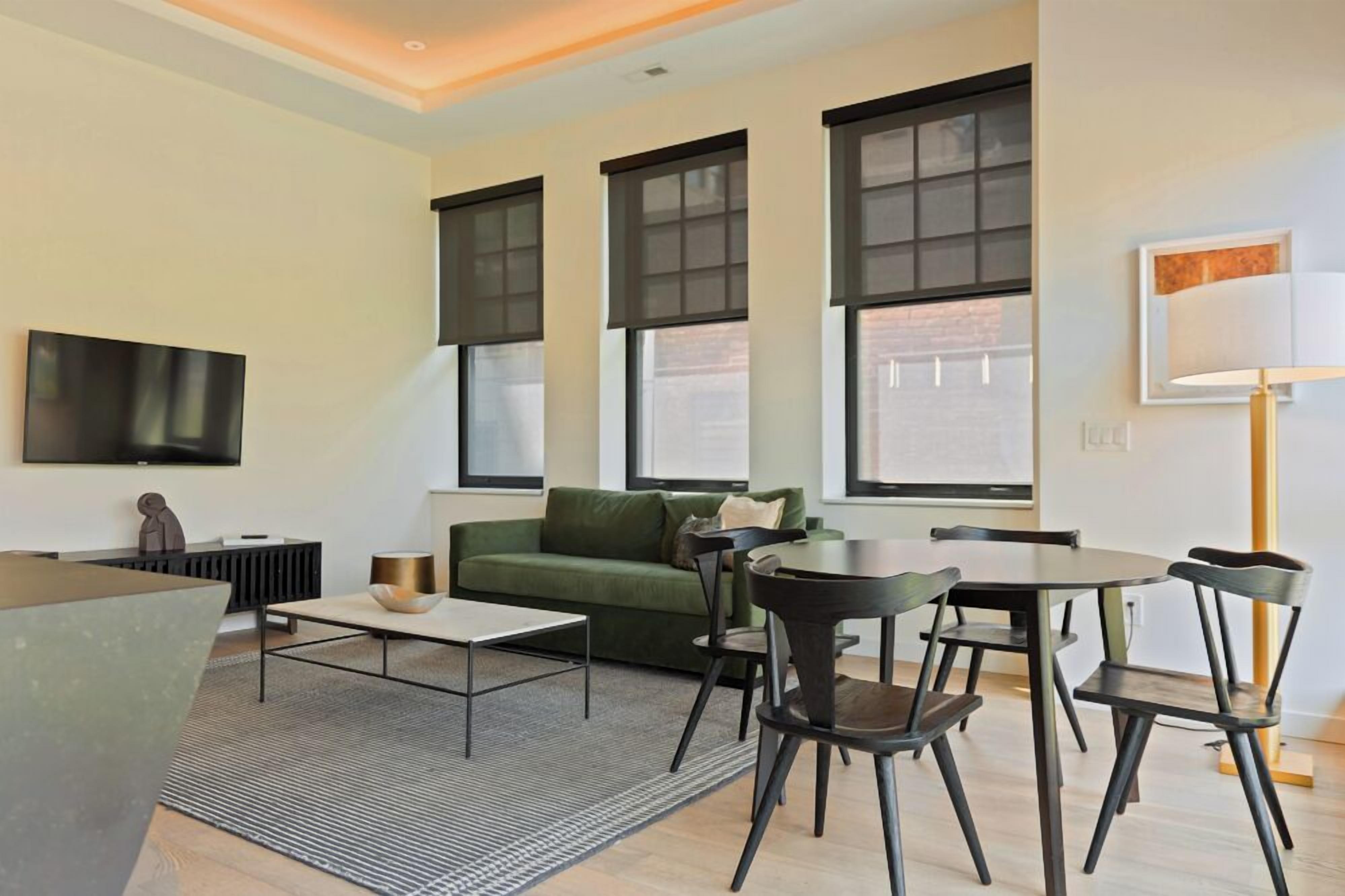 A modern living room with a green sofa, a coffee table, and a dining area with chairs and a table.
