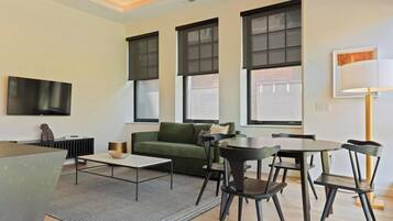 A modern living room with a green sofa, a coffee table, and a dining area with chairs and a table.