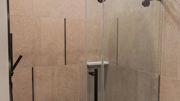 A glass-enclosed shower stall with a handheld showerhead, a vertical rain bar, and a wall-mounted towel rack.