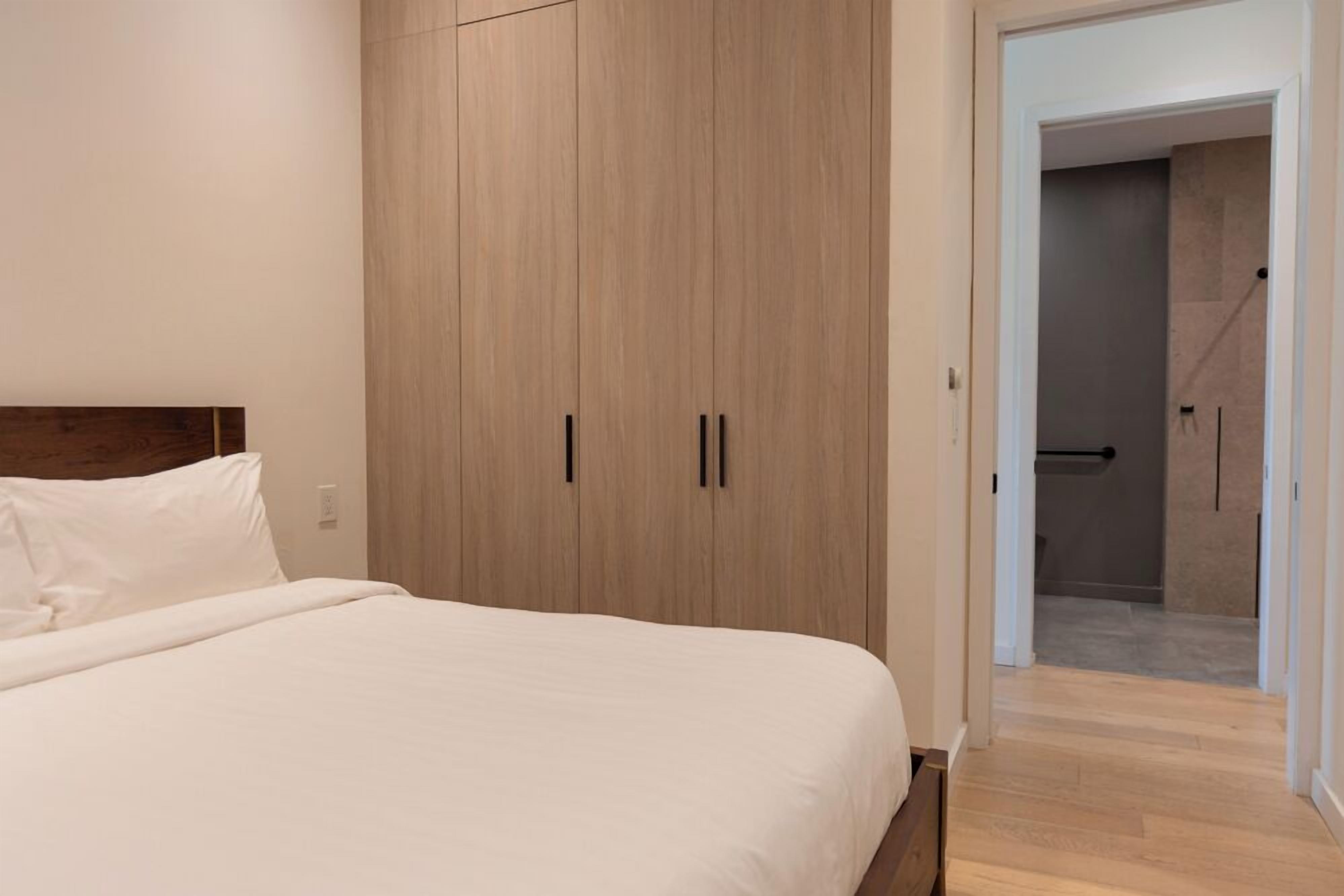 Un dormitorio con una cama grande, un armario de madera y un baño visible a través de una puerta abierta.