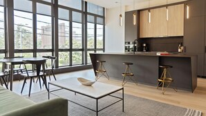 A modern kitchen with large windows, a central island, bar stools, and a dining area with a table and chairs. - Sosuite at The Onyx - Museum District (Philadelphia)