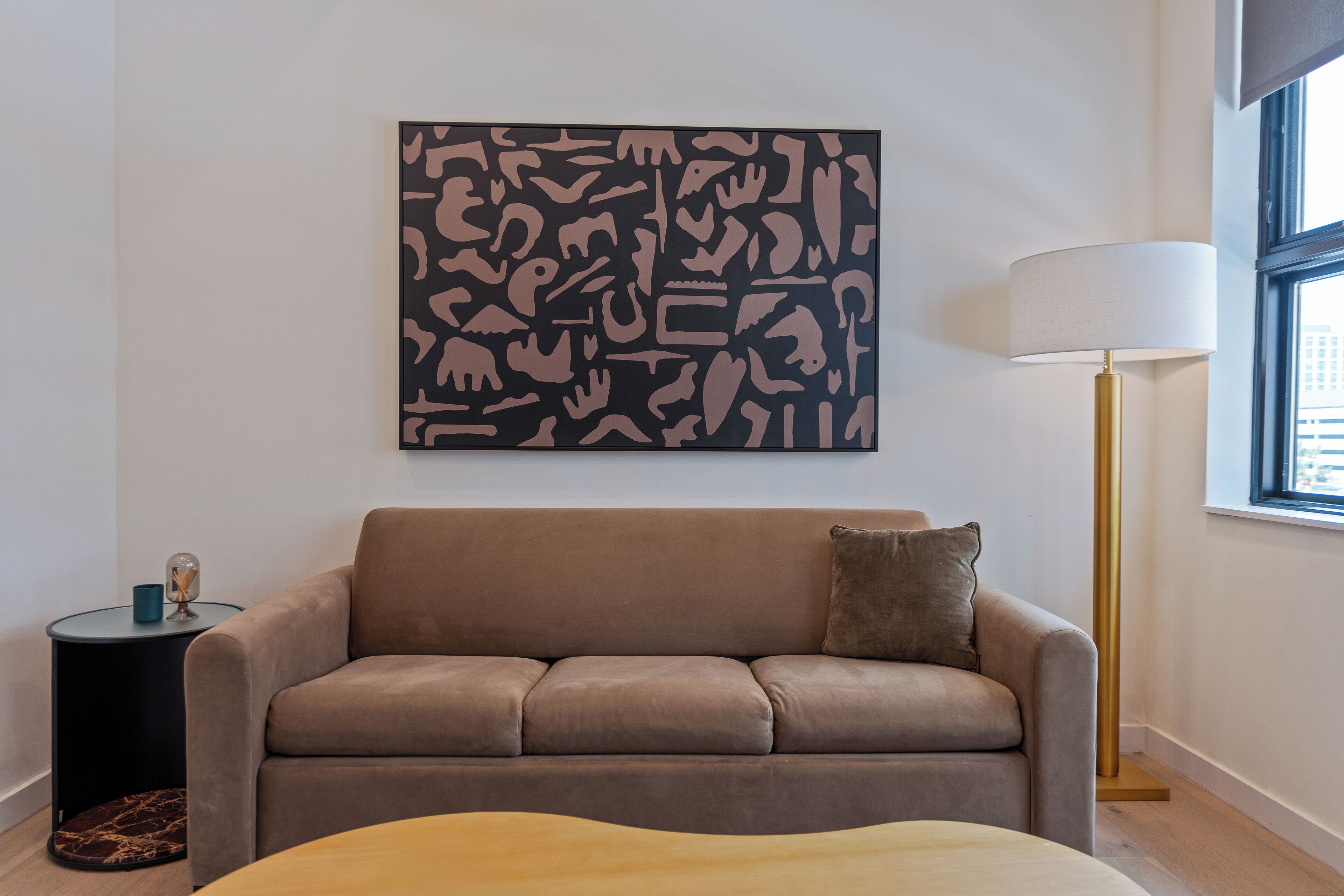 A modern living room with a brown sofa, a side table, a floor lamp, and a large abstract artwork on the wall.