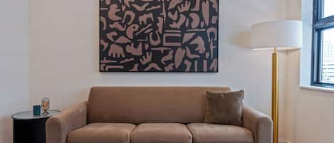 A modern living room with a brown sofa, a side table, a floor lamp, and a large abstract artwork on the wall.