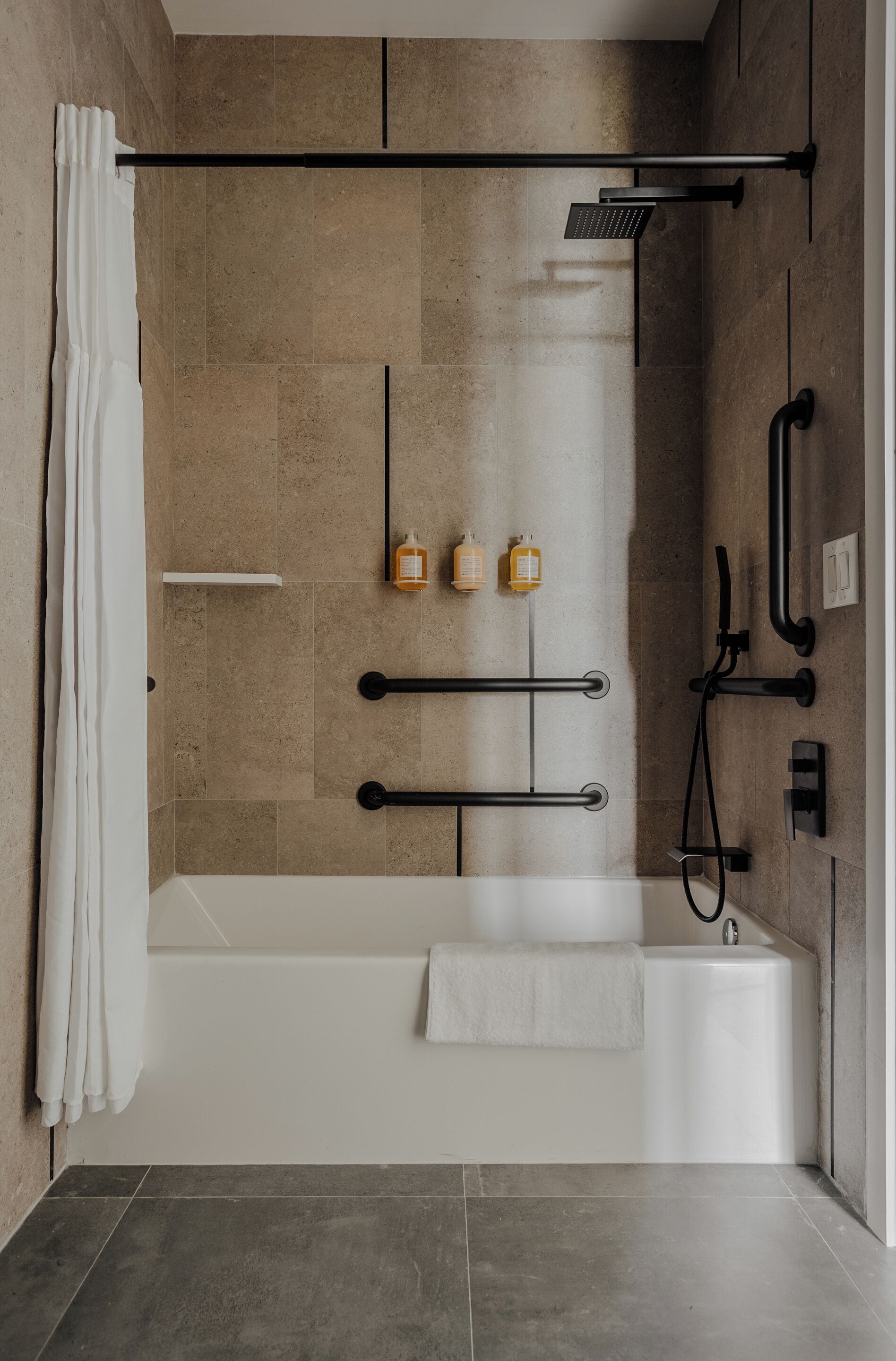 A modern shower area with a bathtub, a showerhead, and handrails.
