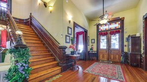 A wooden staircase with a floral arrangement at the bottom, a red rug in the center, and a chandelier above. - 'Grand Gables' Home: 1 Block to St Johns River! (Palatka)