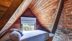 A small, cozy attic bedroom with a sloped ceiling, a single bed, and a window with a white blind. - 'Grand Gables' Home: 1 Block to St Johns River! (Palatka)