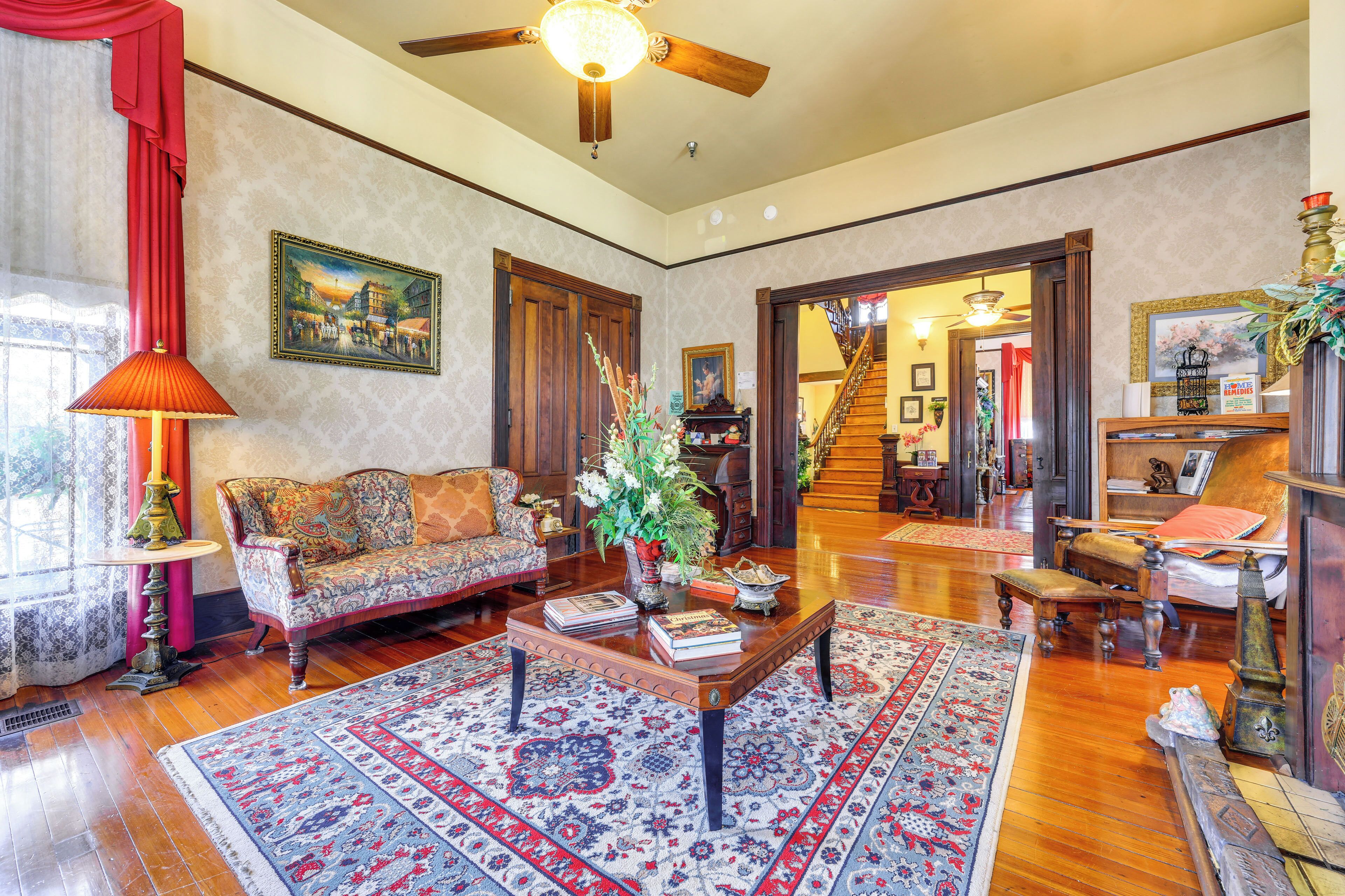 A spacious living room with a wooden floor, a large sofa, a coffee table with books, and a staircase leading to another level.