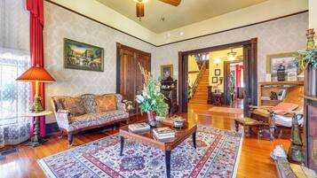 A spacious living room with a wooden floor, a large sofa, a coffee table with books, and a staircase leading to another level.