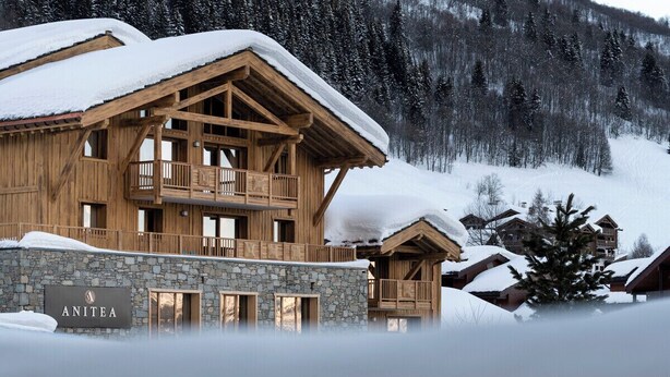 Un chalet en bois, avec des fondations en pierre, un balcon et une enseigne portant l’inscription « ANITEA ».