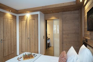 Une chambre avec des murs lambrés en bois, un lit agrémenté d’oreillers blancs et à motifs, et un jeu d’échecs posé sur le lit.