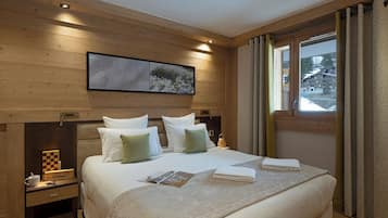 Una habitación de hotel con cabecera de madera, una cama grande con almohadas blancas y verdes, una mesita de noche con lámpara y una ventana con cortinas.