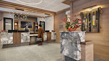 Un moderno vestíbulo de hotel con mostradores de recepción de mármol, paneles de madera y una gran planta decorativa.