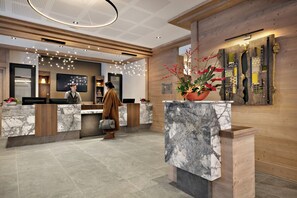 Un moderno vestíbulo de hotel con mostradores de recepción de mármol, paneles de madera y una gran planta decorativa.