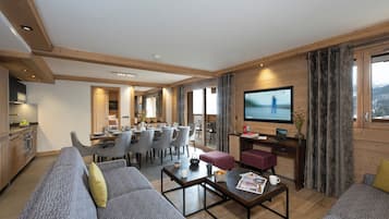 Un vaste espace de vie comprenant un canapé, une table basse et un téléviseur. On y trouve également un coin repas avec des chaises et une table, ainsi qu’une cuisine à l’arrière-plan.