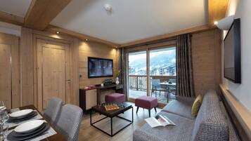 Una sala moderna con techo de madera, un televisor de pantalla plana, un comedor con mesa dispuesta para cuatro personas y un balcón con vistas a la ciudad.