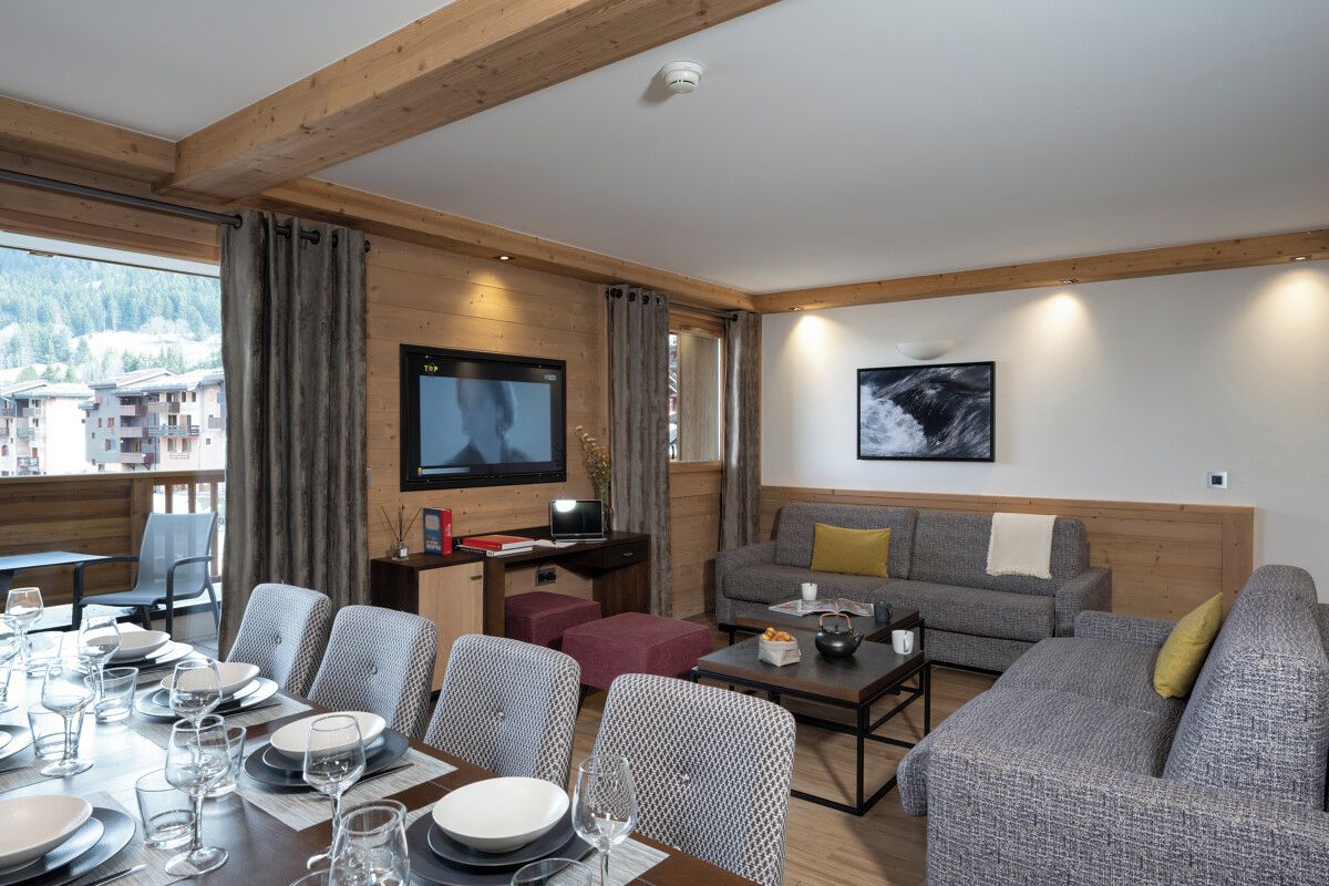 Un salon moderne avec un coin repas, des poutres en bois, un téléviseur à écran plat et une vue sur les montagnes.