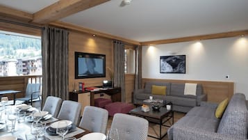 Un salon moderne avec un coin repas, des poutres en bois, un téléviseur à écran plat et une vue sur les montagnes.