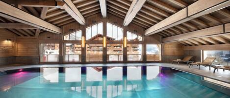 A large indoor swimming pool with wooden beams and large windows.
