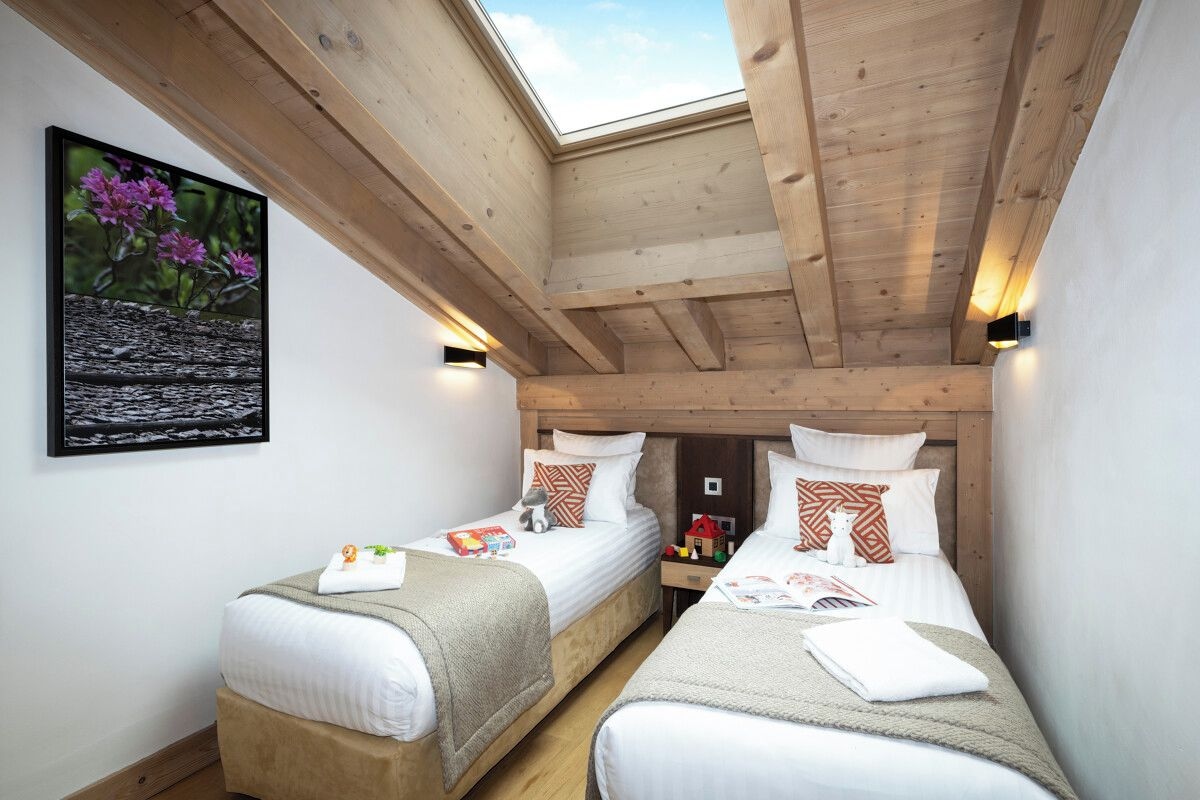 Una habitación con dos camas individuales, vigas de madera, un tragaluz y un cuadro enmarcado en la pared.