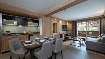 A modern kitchen with wooden beams, a dining area with a table set for four, and a living area with a sofa and a balcony with a view of buildings.
