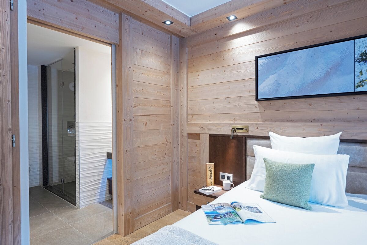 Un dormitorio moderno con paneles de madera, una cama con almohadas blancas y verdes, una mesita de noche con una lámpara y un cuadro enmarcado en la pared.