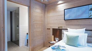 A modern bedroom with wooden paneling, a bed with white and green pillows, a bedside table with a lamp, and a framed picture on the wall.