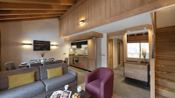 Un salon moderne avec un canapé, des fauteuils et une table basse. On y trouve également un coin cuisine avec des meubles en bois et un coin repas avec des tables et des chaises.