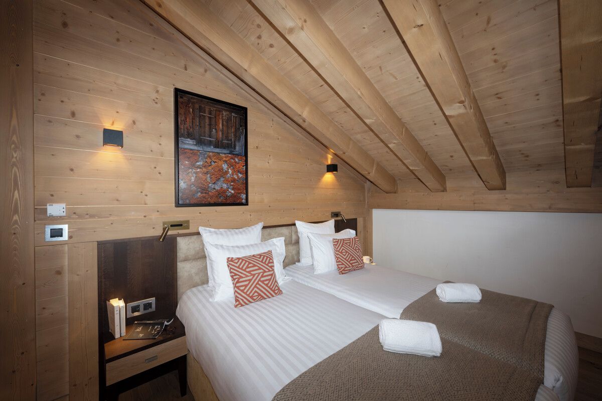 A wooden cabin room with two beds, a painting on the wall, and two wall-mounted lights.