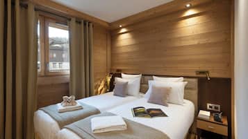 Une chambre aux murs lambrissés, avec deux lits, une table de chevet et une fenêtre avec des rideaux.