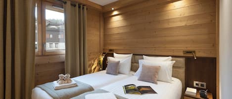 Une chambre aux murs lambrissés, avec deux lits, une table de chevet et une fenêtre avec des rideaux.
