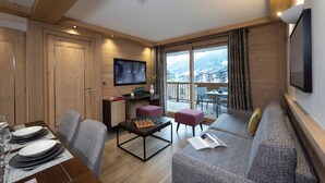 Un salon moderne avec un plafond en bois, un téléviseur à écran plat, un coin repas avec une table dressée pour quatre personnes et un balcon offrant une vue sur la ville.