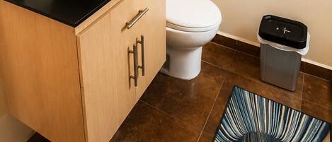 A modern bathroom with a large mirror, a white sink, a toilet, and a trash bin.