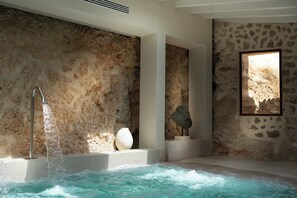 Un espace de détente avec un mur en pierre, un jacuzzi et un grand vase.