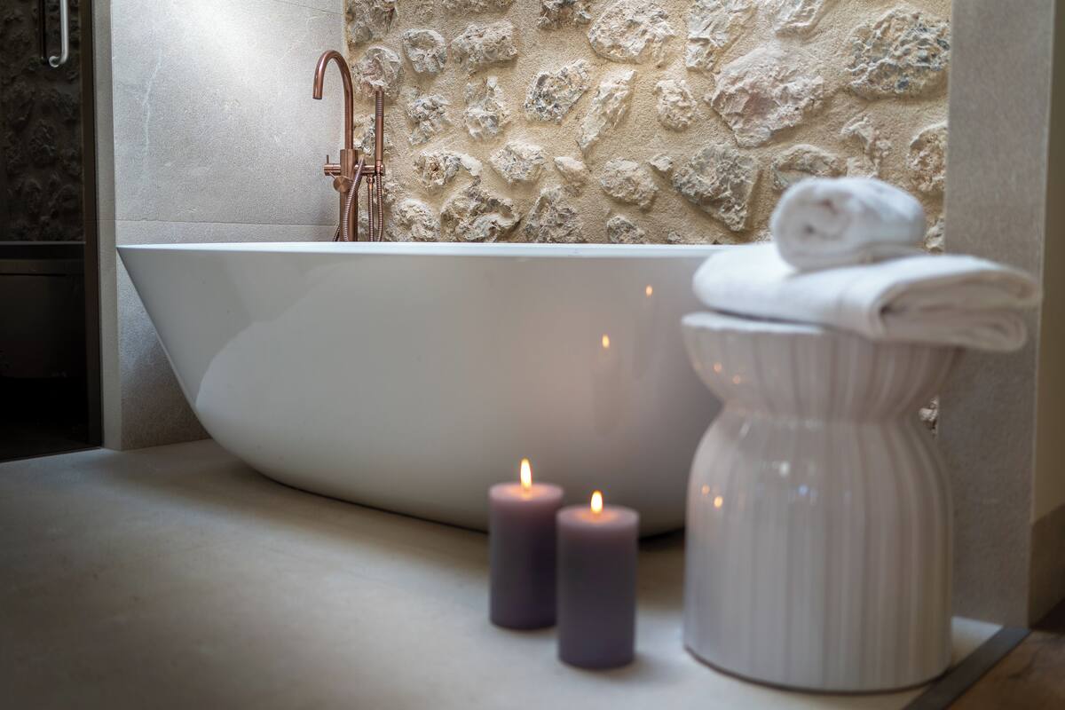 A modern bathroom with a freestanding bathtub, a stone-textured wall, and two lit candles on a countertop.