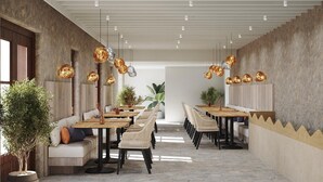 Un espace repas moderne doté de hauts plafonds, de murs en briques apparentes et d’un éclairage suspendu. Les tables sont disposées pour les repas, avec des chaises et un canapé.