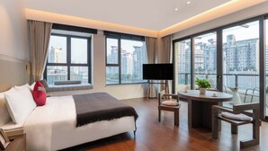 Une chambre d’hôtel moderne, dotée d’un grand lit, d’une télévision, d’une petite table avec une plante et d’un balcon offrant une vue sur la ville.