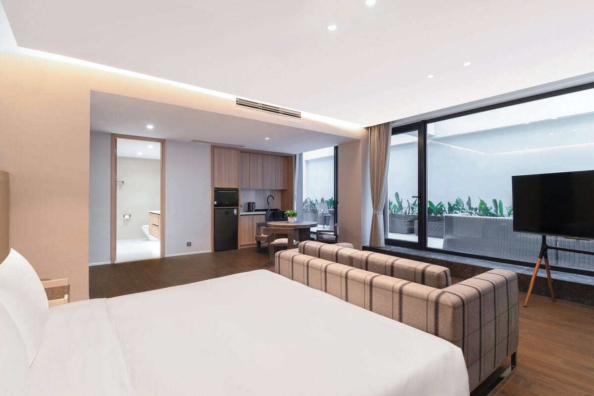 Ein modernes Hotelzimmer mit einem großen Bett, einem Sofa, einem Fernseher und einem Balkon mit Blick.