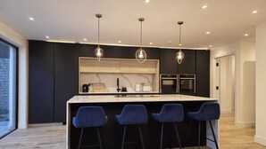 A modern kitchen with a central island, bar stools, and pendant lighting.