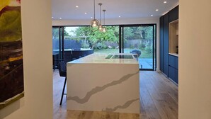 A modern kitchen with a central island, large windows, and a view of the outdoors.