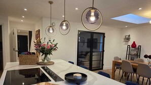 A modern kitchen with a central island, pendant lighting, and a dining area with a glass door leading to a living space.