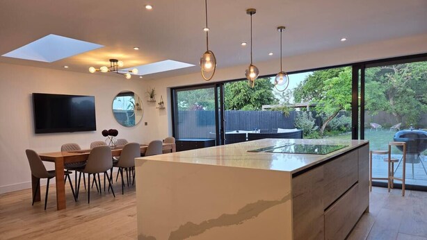 A modern kitchen with a large island, dining area with chairs, and a large window with a view of the outdoors.