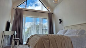 A bedroom with a large window, a bed, a desk, and a chair.