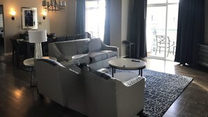 A modern living room with a sofa, a coffee table, and a chandelier. There is a dining area with chairs and a table, and a balcony with a view. - Wyndham Oceanside Pier Resort - 3 Bedroom Ocean View Presidential Suite - Ocean (Oceanside)