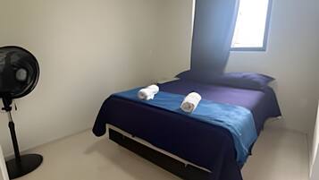 A bedroom with a bed, a standing fan, and a window with curtains.