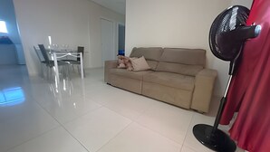 Ein modernes Wohnzimmer mit einem beigefarbenen Sofa, einem Esstisch mit Stühlen und einem Standventilator.