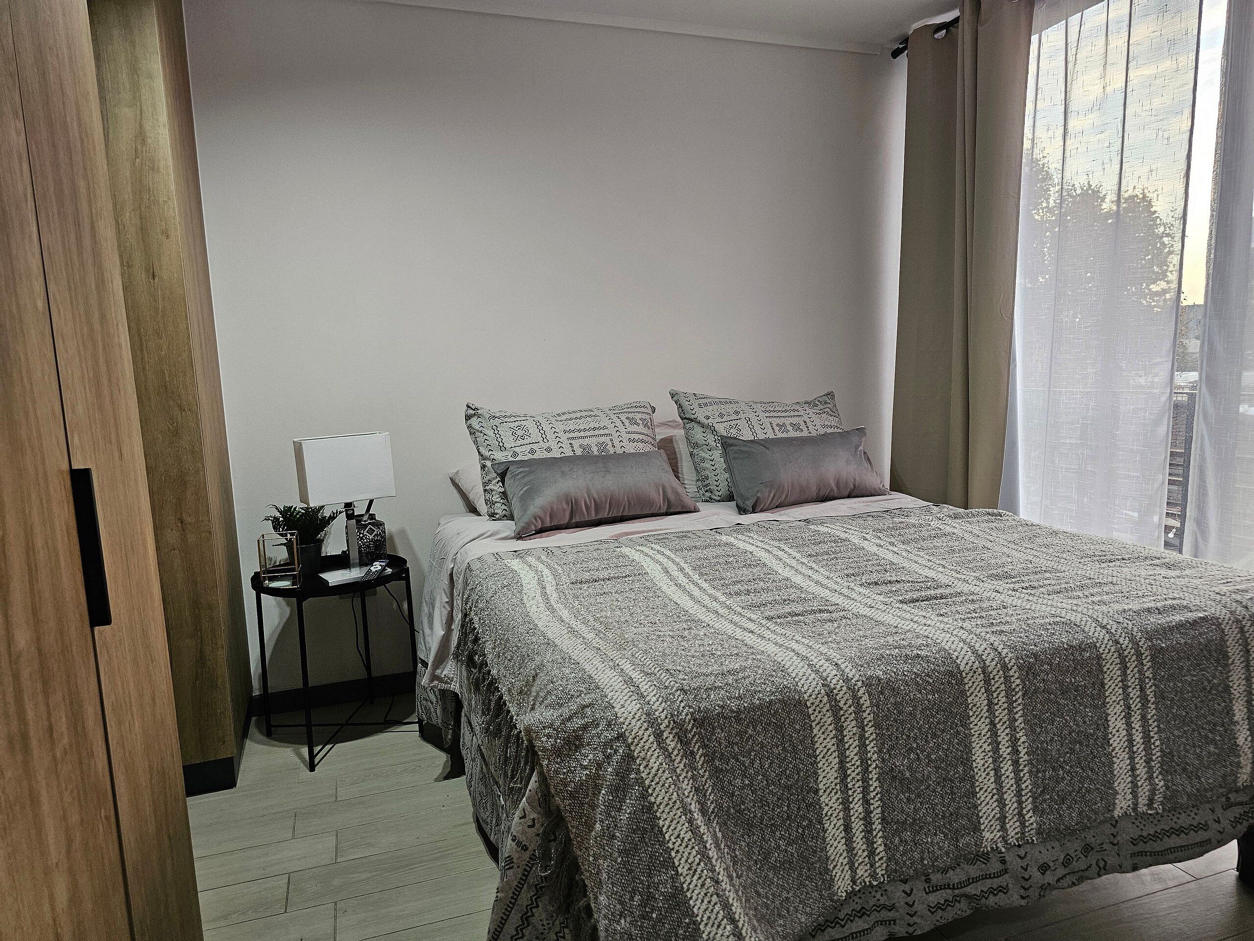 A bedroom with a bed, bedside table, lamp, and curtains.