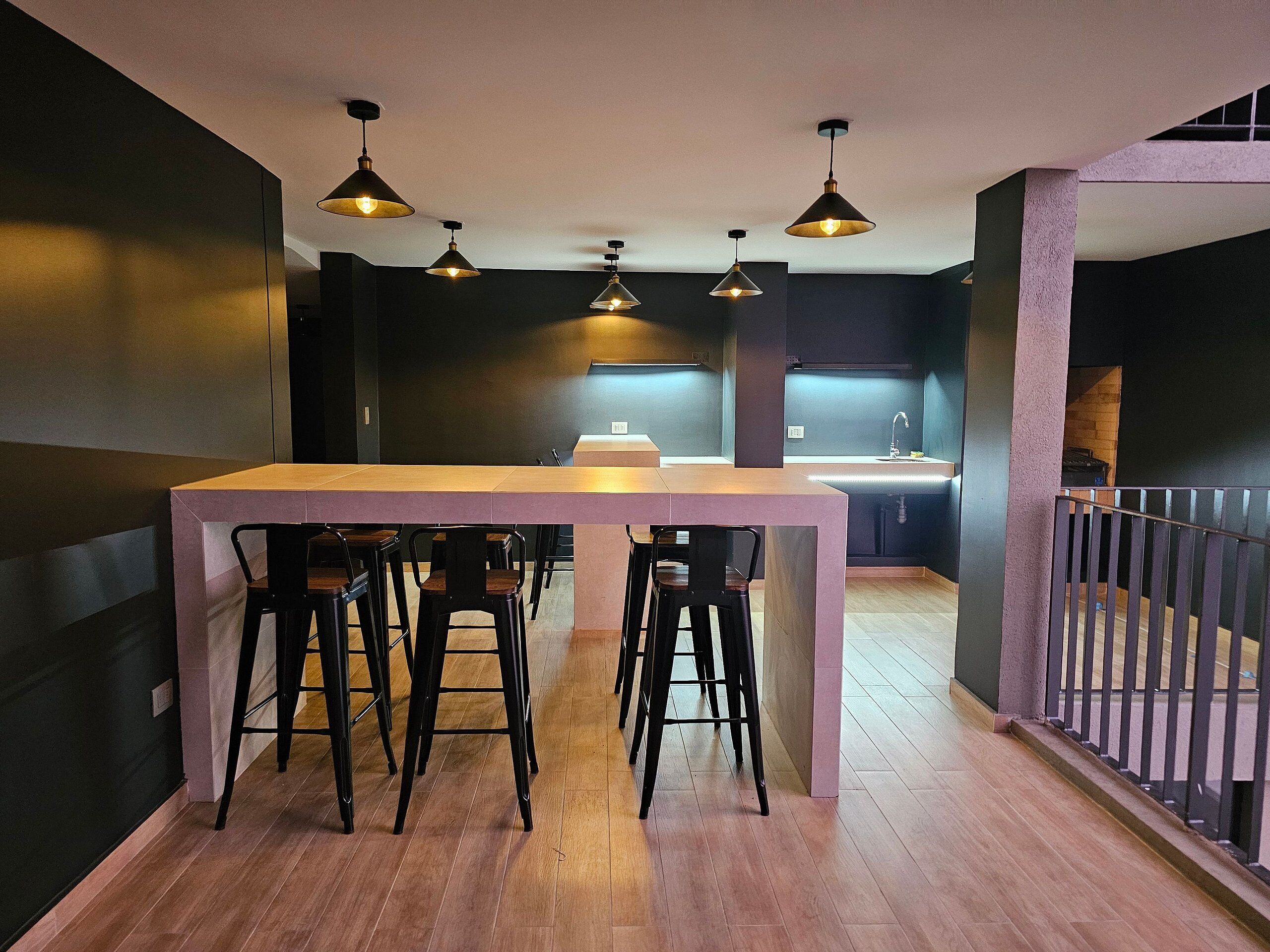 A modern kitchen with a central island, bar stools, pendant lighting, and a view of the living area.