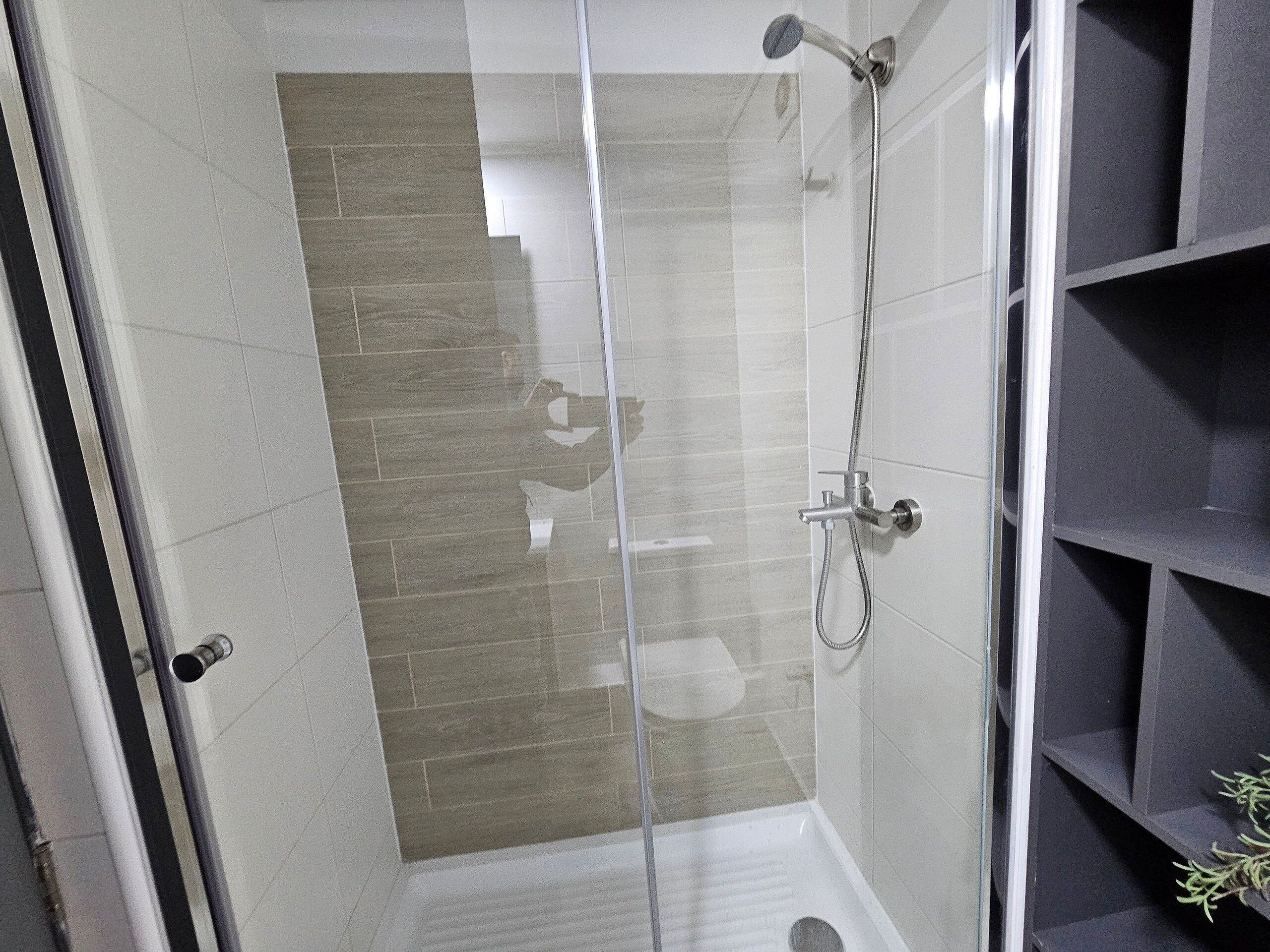 A glass-enclosed shower with a handheld showerhead and a wall-mounted faucet.