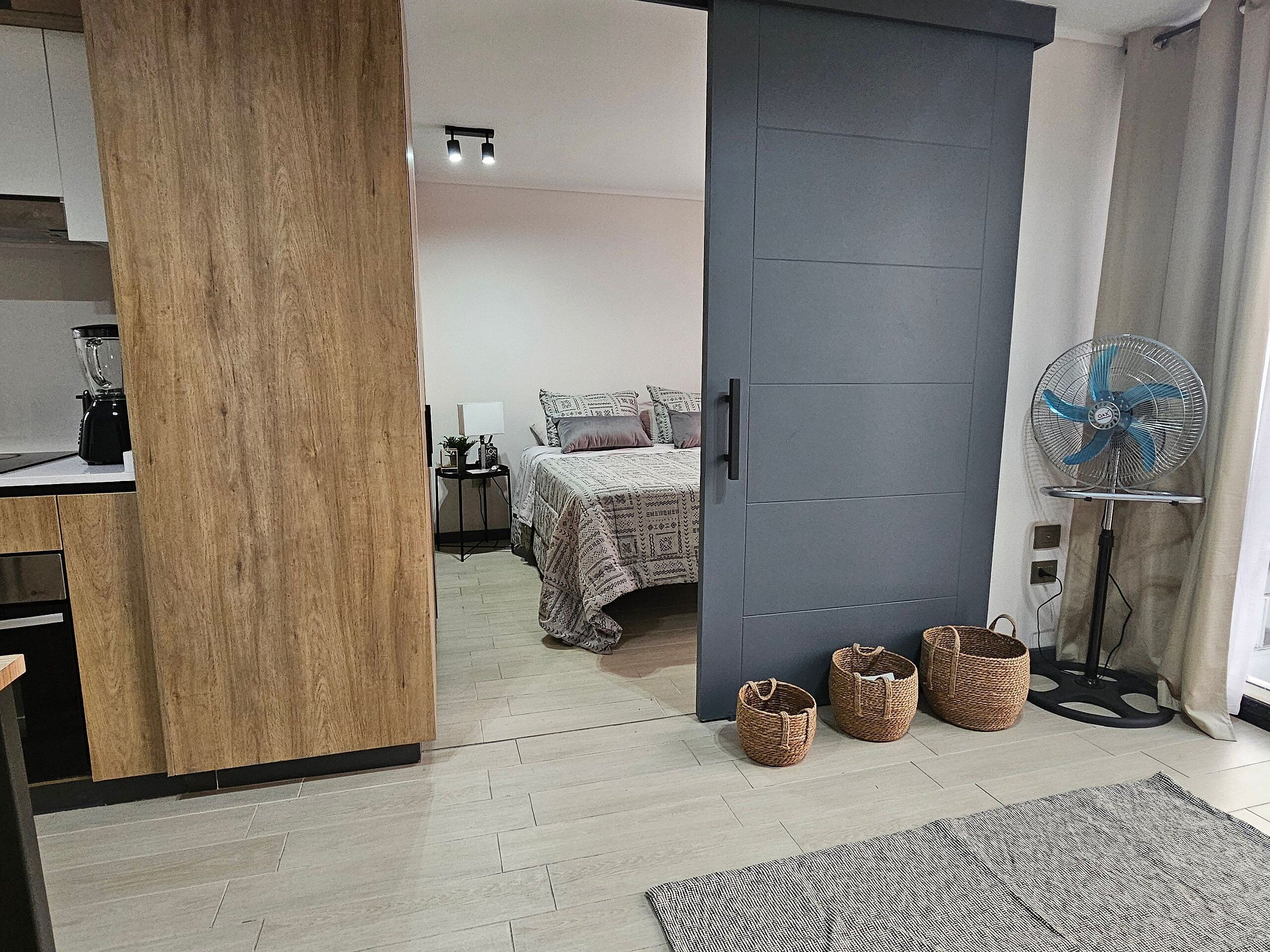 Un dormitorio moderno con cama, mesita de noche, lámpara y un ventilador de pie.