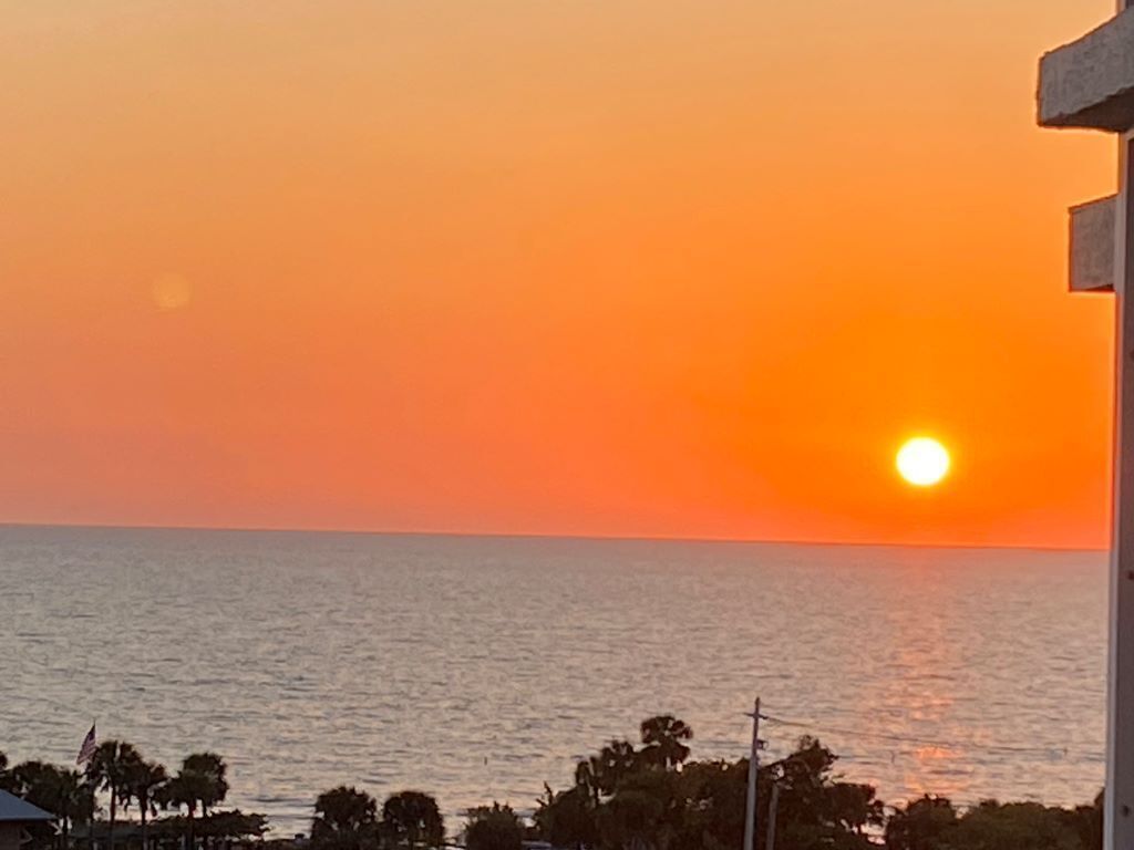 A sunset over a body of water with a silhouette of trees and a building in the foreground.